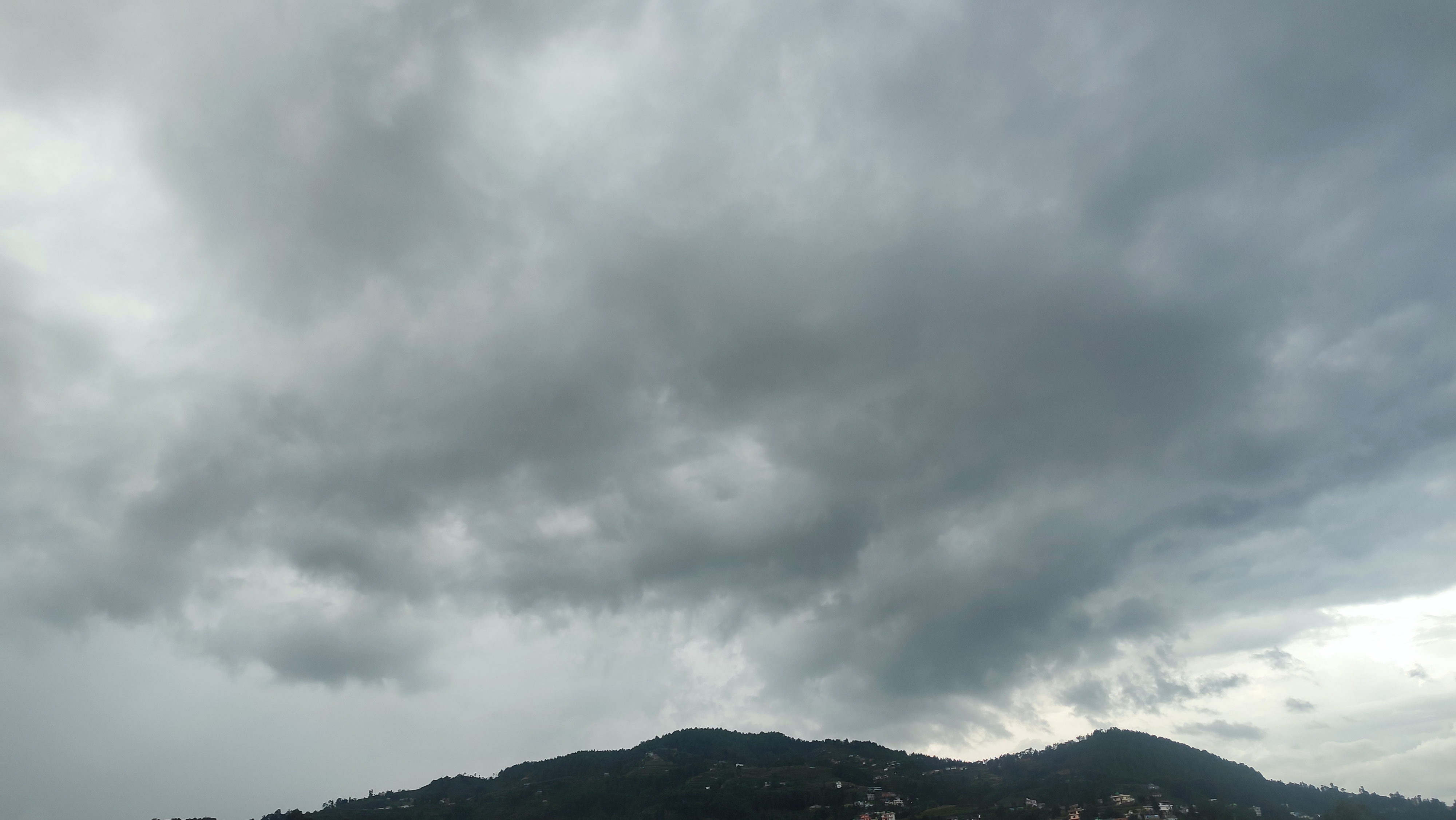 Dark storm clouds over green mountains with scattered houses.