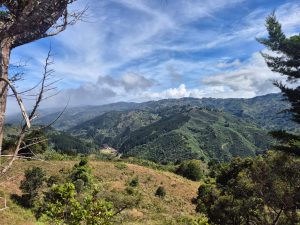 Mountain landscape with green hills, forests, and a blue sky with white and gray clouds.