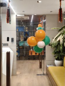 Modern room decorated with orange, green, and white balloons, a potted plant, and a shelf of trophies.