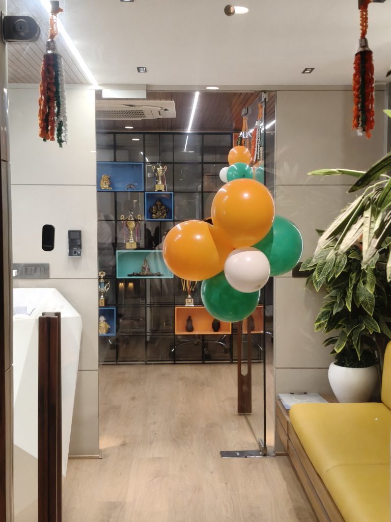 Modern room decorated with orange, green, and white balloons, a potted plant, and a shelf of trophies.