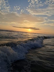 Sunset at the beach with gentle waves, orange and golden light, and wispy clouds in the sky.