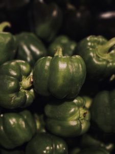 Fresh green bell peppers are arranged closely together, with one large pepper standing out in the center. Soft lighting and shallow focus highlight its smooth surface, rounded shape, and natural green color. Captured in Palazhi, Kozhikode, Kerala.