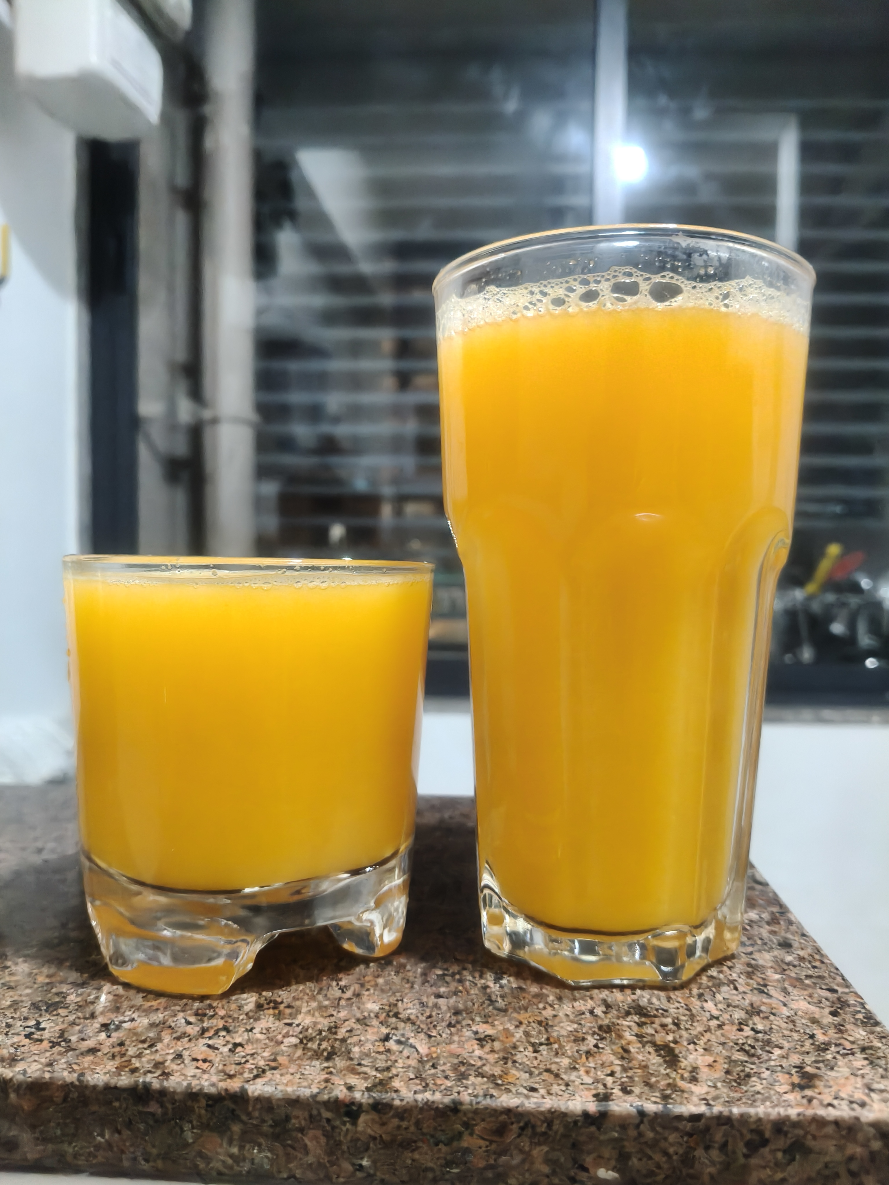 Two glasses of fresh orange juice on a kitchen counter.