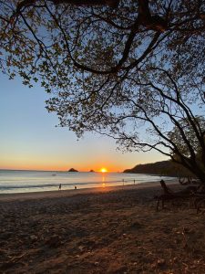 Sunset over a calm beach with gentle waves and warm orange skies.