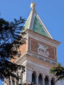 Top of St Mark's Campanile bell tower in Venice featuring the golden angel weather vane and the relief of the winged Lion of St Mark.