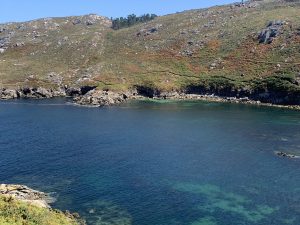Panoramic view of A Barda Bay along the Camiño dos Faros, with deep blue and turquoise water and a rugged coastline in the background.