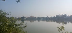 A calm lake reflecting buildings and trees on a peaceful morning under a clear sky.