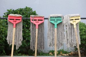 Four mops hanging in a row, positioned to dry against a rod.