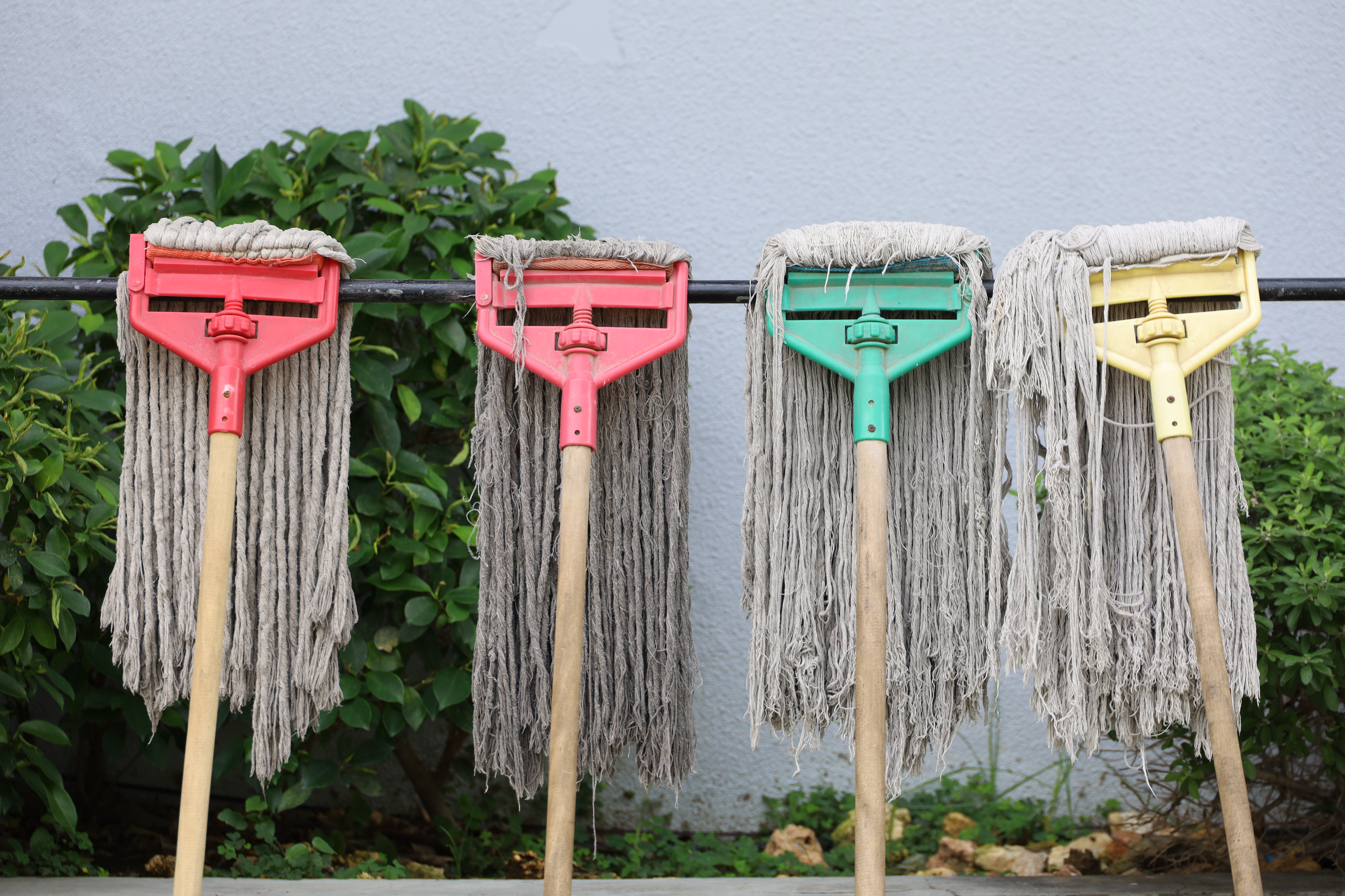 Four mops hanging in a row, positioned to dry against a rod.