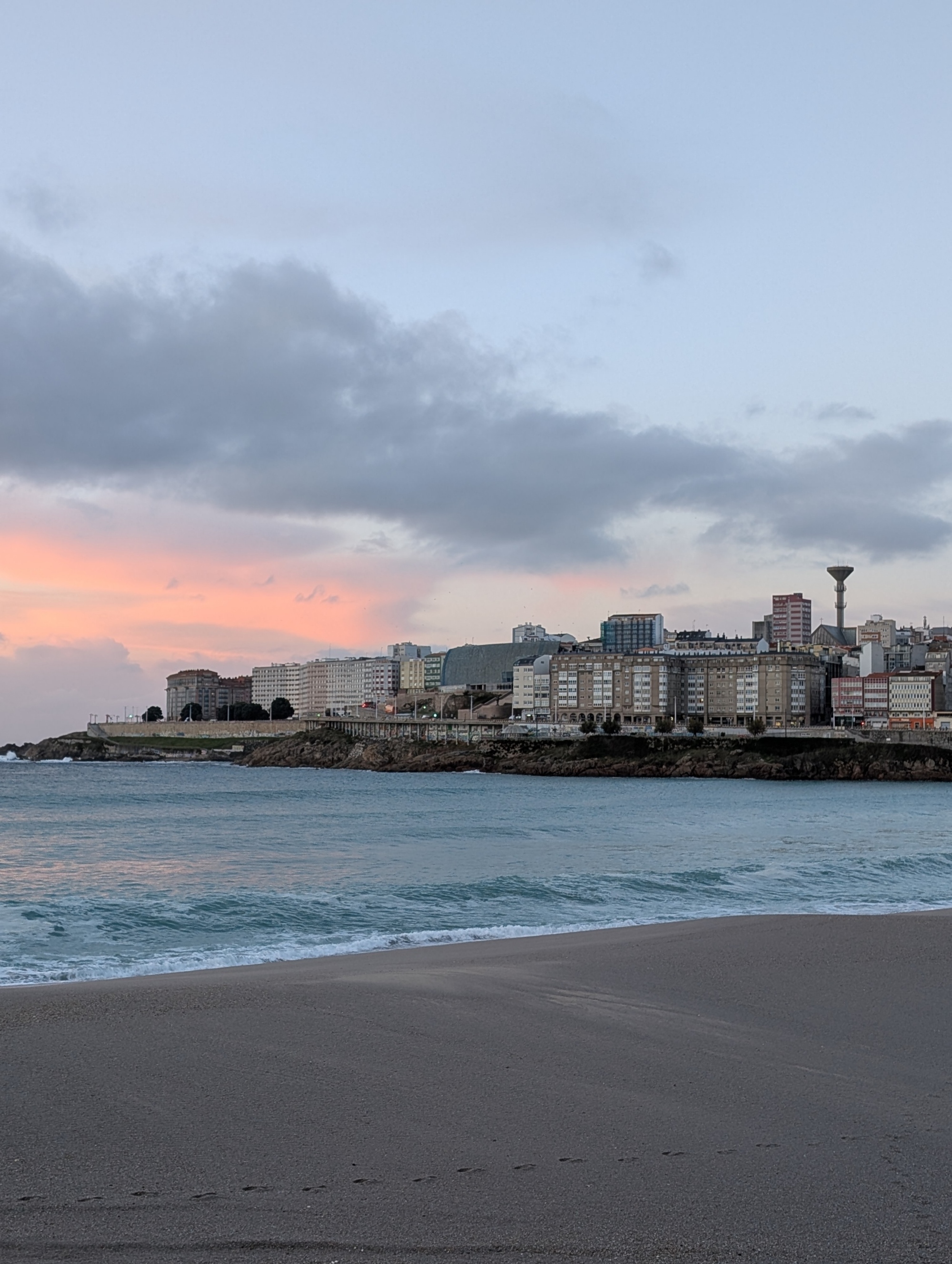 Twilight sunset over a beach showing soft pink sky tones, Atlantic waves, and the city skyline.