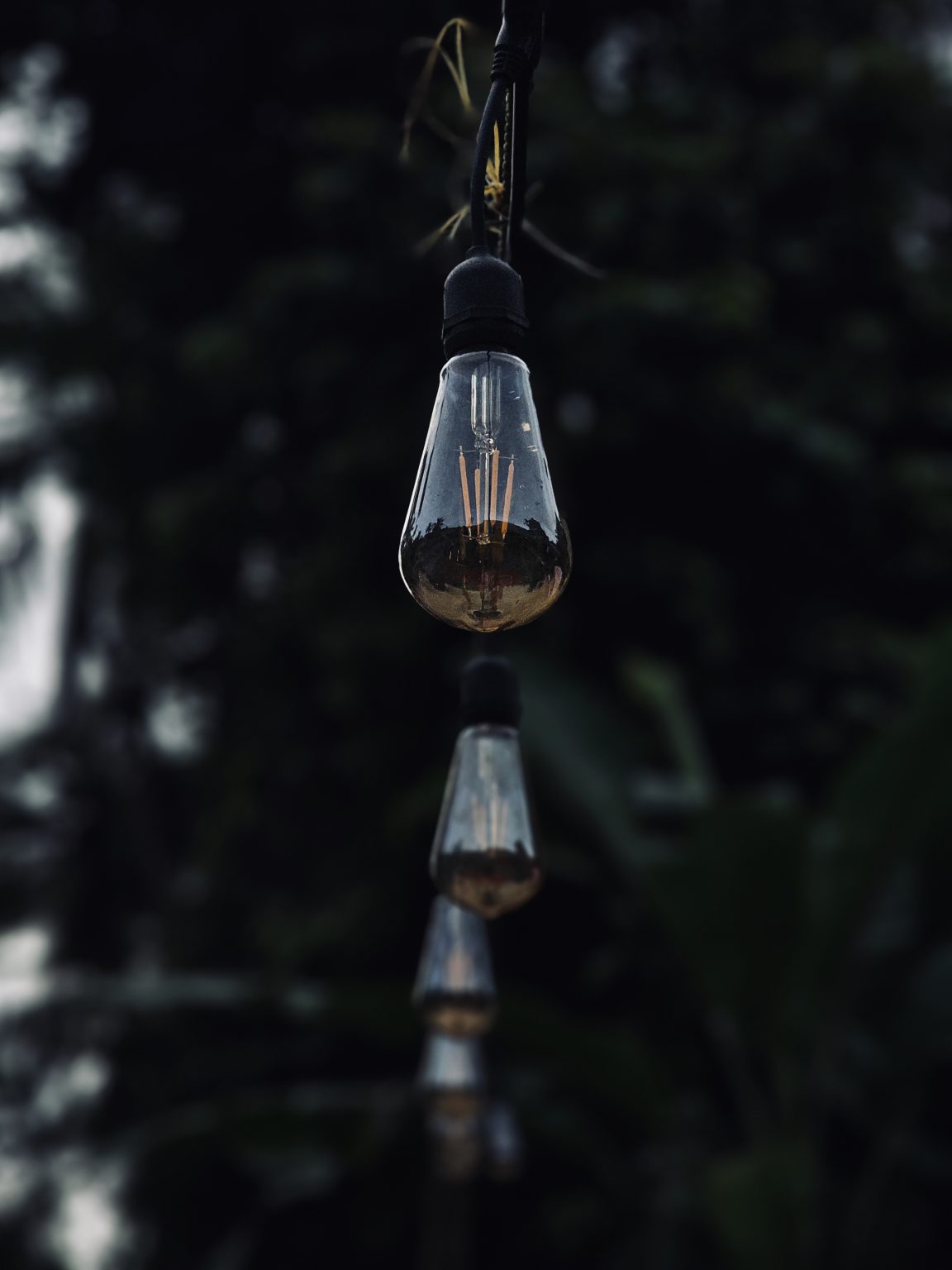 A row of hanging decorative bulbs creates a simple and elegant scene. The sharp focus on the front bulb and the soft blur behind it add depth and mood. Captured in Peruvayal, Kozhikode, Kerala.