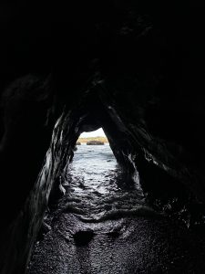 
Sea cave with a small beach and coastal view in the background.