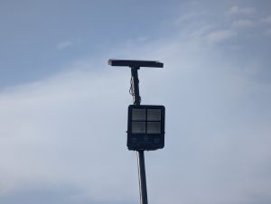 A black solar streetlight mounted on a tall pole under a clear blue sky.
