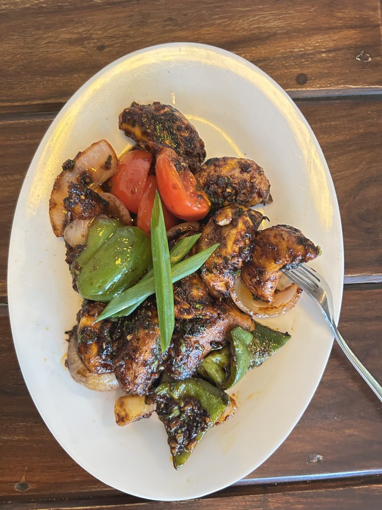 A white oval plate filled with grilled chicken pieces that are dark and charred, indicating they are well-cooked and seasoned.