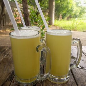 Three clear mugs of fresh sugarcane juice on a wooden table.
