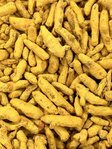 A close-up view of dried turmeric roots fills the frame, showing their natural shapes, rough texture, and bright golden-yellow color. The repeating forms create a simple but striking natural pattern. Captured in Kuttikkattoor, Kozhikode, Kerala.