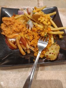 A black square plate holds a colorful mix of food.

