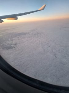 Airplane wing above a sea of clouds, illuminated by warm sunset light.