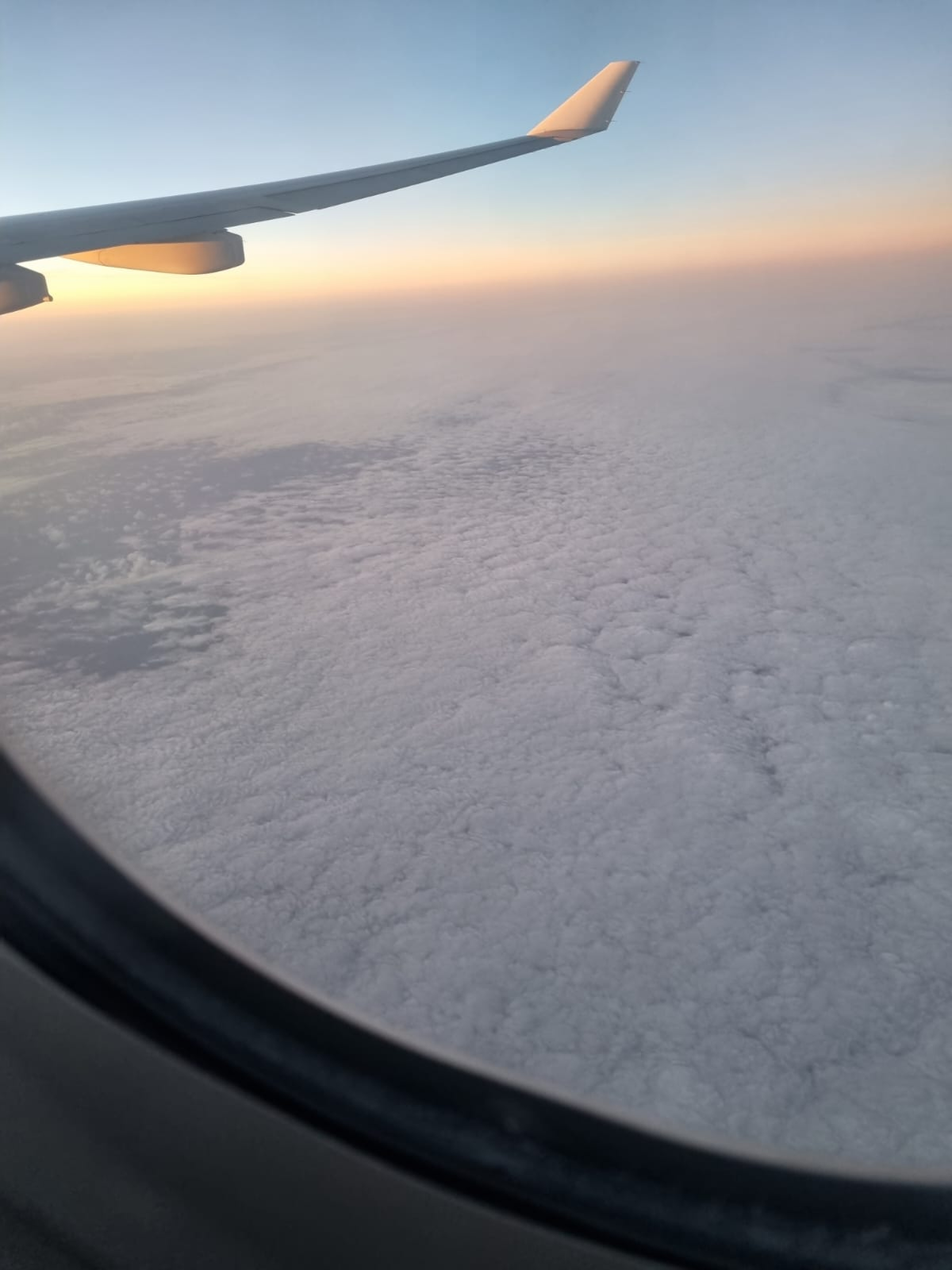Airplane wing above a sea of clouds, illuminated by warm sunset light.