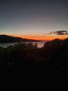 Sunset over the sea with orange and golden light, silhouetted mountains, and reflections on the water.