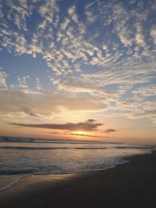 Sunset over a beach with colorful skies, soft clouds, and warm sunlight reflecting on the water.