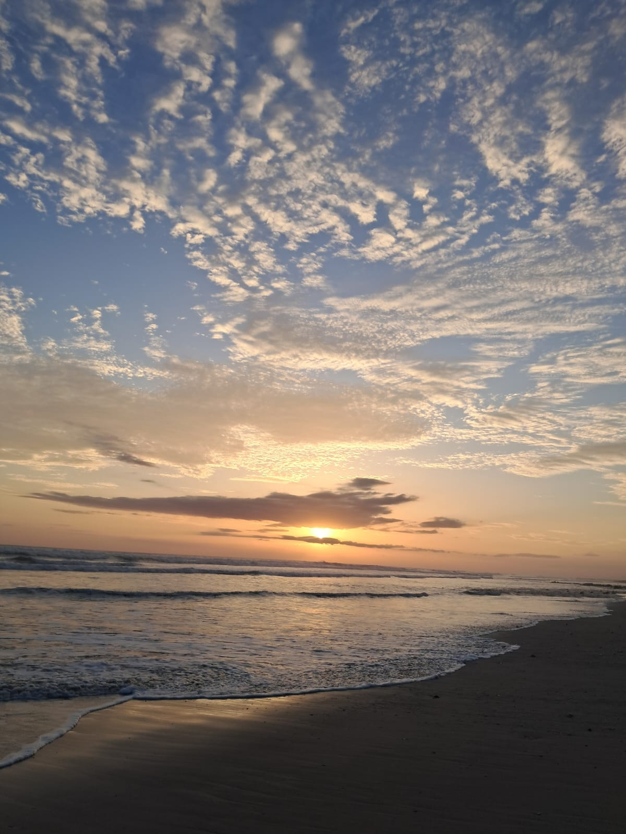 Sunset over a beach with colorful skies, soft clouds, and warm sunlight reflecting on the water.