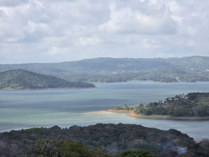 Layers of forested hills surround a tranquil lake, where changing light and scattered clouds reveal the rich colors and contours of the landscape