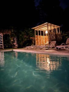 
Peaceful pool at night with lounge chairs, tropical greenery, and warm lights.