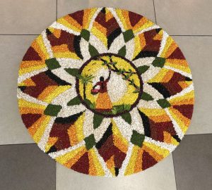 A colorful circular floral arrangement featuring a traditional figure holding a basket, surrounded by vibrant petal patterns.