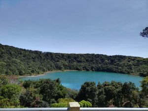 
A serene and tranquil landscape features a large, calm lake surrounded by lush green hills and dense forest.