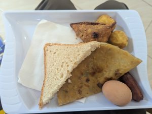 A tray with bread, fried snacks, a boiled egg, and a sausage.
