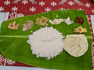 A traditional Kerala meal is served on a fresh banana leaf, with white rice, side dishes, chutneys, vegetables, and a crisp papad. The simple presentation highlights the traditional style of serving food during festive meals. Location: Perumanna, Kozhikode, Kerala.