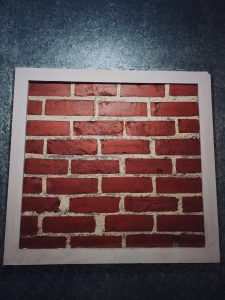 A rectangular panel displays rows of red bricks with uneven textures and pale mortar lines, framed by a dark blue textured wall. The simple geometric pattern creates an interesting study of color, texture, and repetition. Captured in Chalappuram, Kozhikode, Kerala.