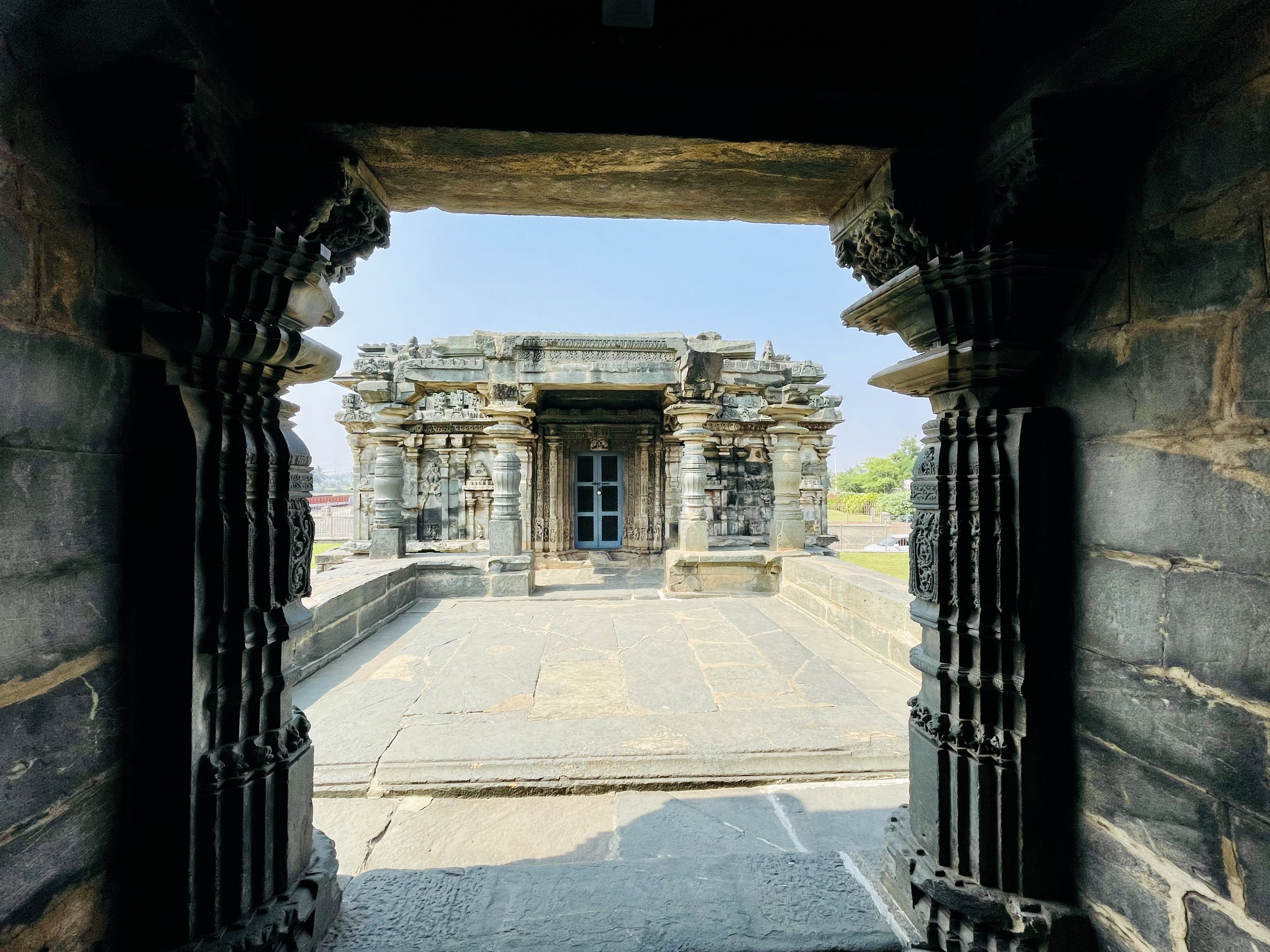 Framed by dark stone pillars, this view looks across the temple courtyard toward another beautifully carved shrine. The natural framing adds depth and draws attention to the temple's elegant architecture. Captured at Kasivisvesvara (also known as Kavatalesvara or Kashivishveshvara) Temple, Lakkundi (Lokkugundi), Gadag district, Karnataka.