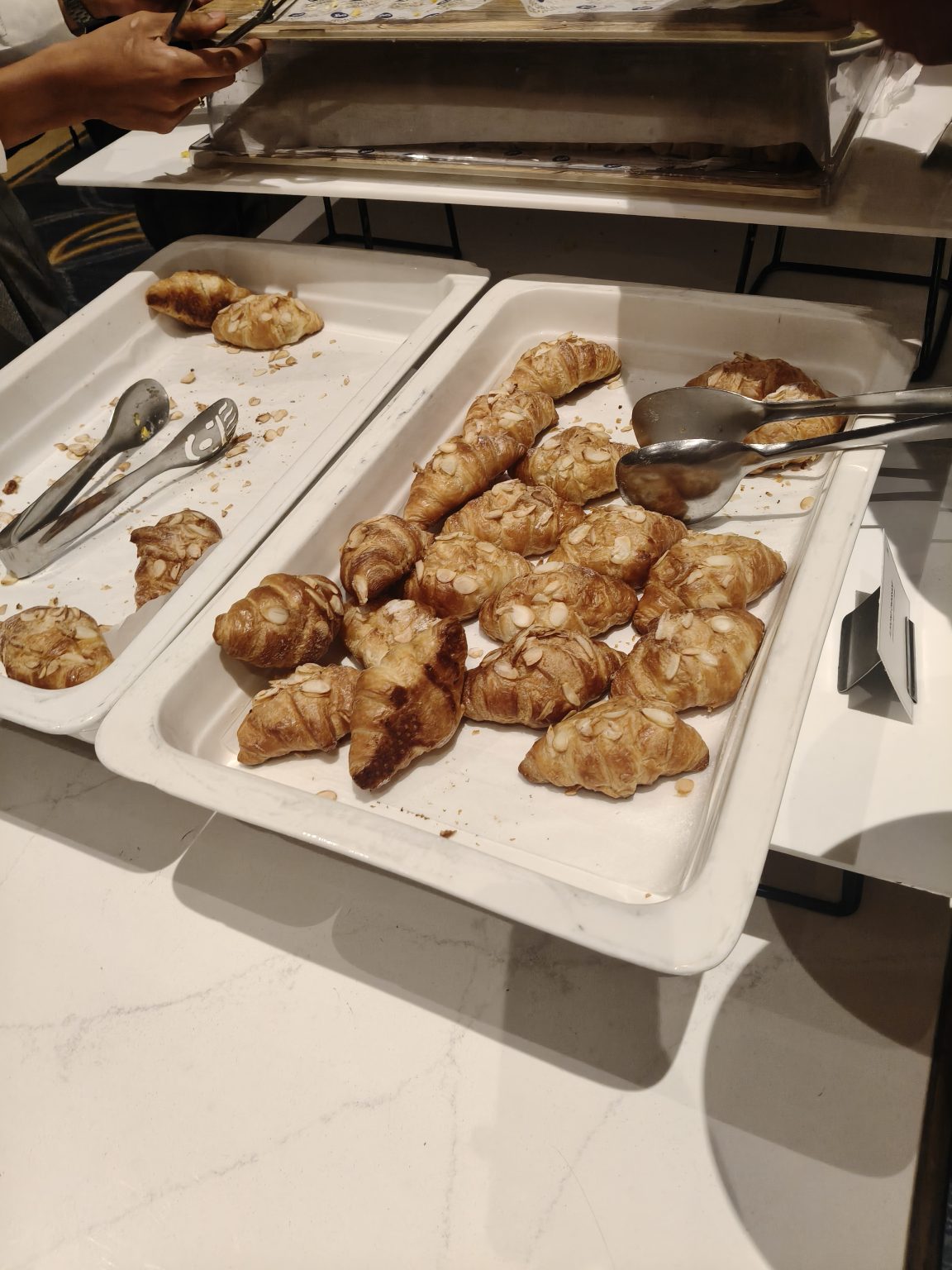 Freshly baked croissants, including almond croissants, served on a buffet tray.