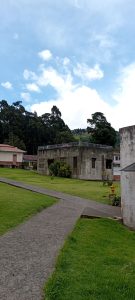 Concrete pathway leading to a weathered building with a rooftop railing at the Sanatorio Durán in Costa Rica, surrounded by open lawn and forested hills.