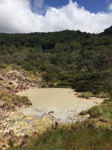 A volcanic landscape surrounded by dense green vegetation, featuring rocky terrain and natural volcanic features.