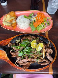 Two plates of food with rice, fried chicken, beef, salad, and lime on a wooden table.