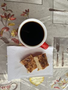 
A cup of coffee with two pieces of bread on a patterned tablecloth.