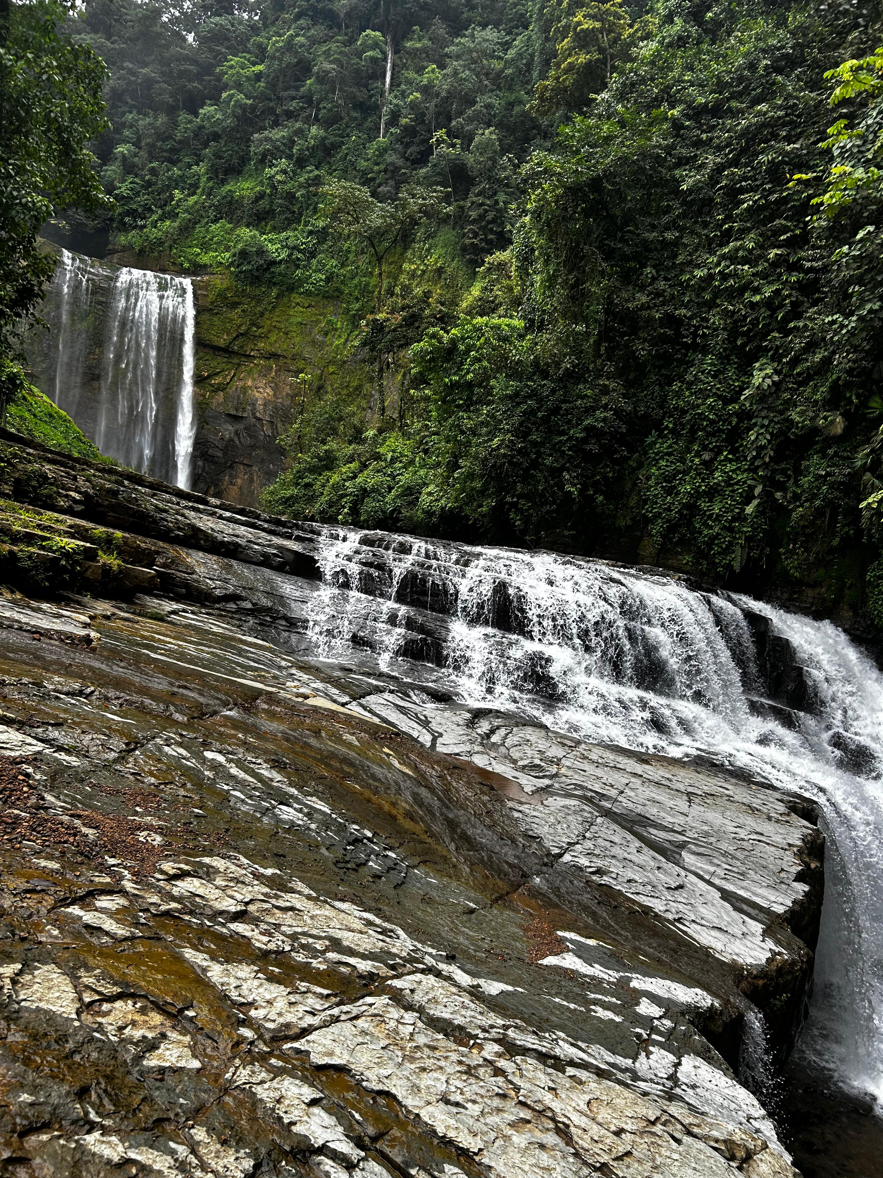 A waterfall flows down a moss-covered rocky cliff into clear pools below.