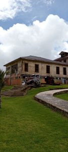 Rusted antique vehicles displayed on the lawn beside a wooden pavilion at the Sanatorio Durán in Costa Rica, with stone steps leading up to the weathered building.