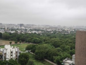 
A panoramic view of a city with green trees, buildings, and a cloudy sky.