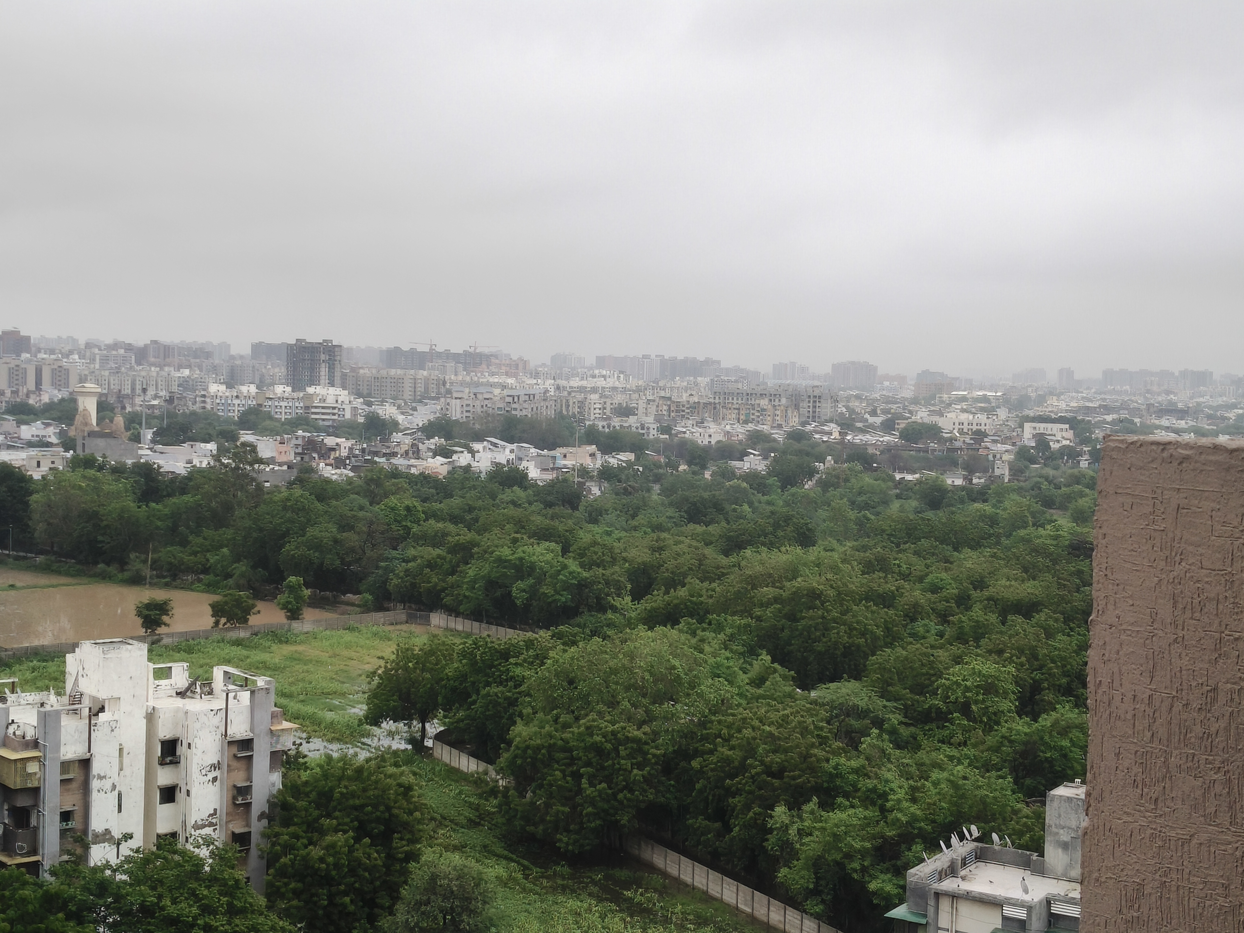 A panoramic view of a city with green trees, buildings, and a cloudy sky.