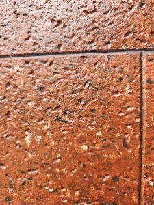 Close-up of a rough reddish-brown surface with small indentations, dark spots, and faint grid-like lines.