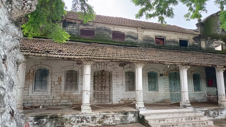 Old traditional building with a tiled roof and a large tree in front.