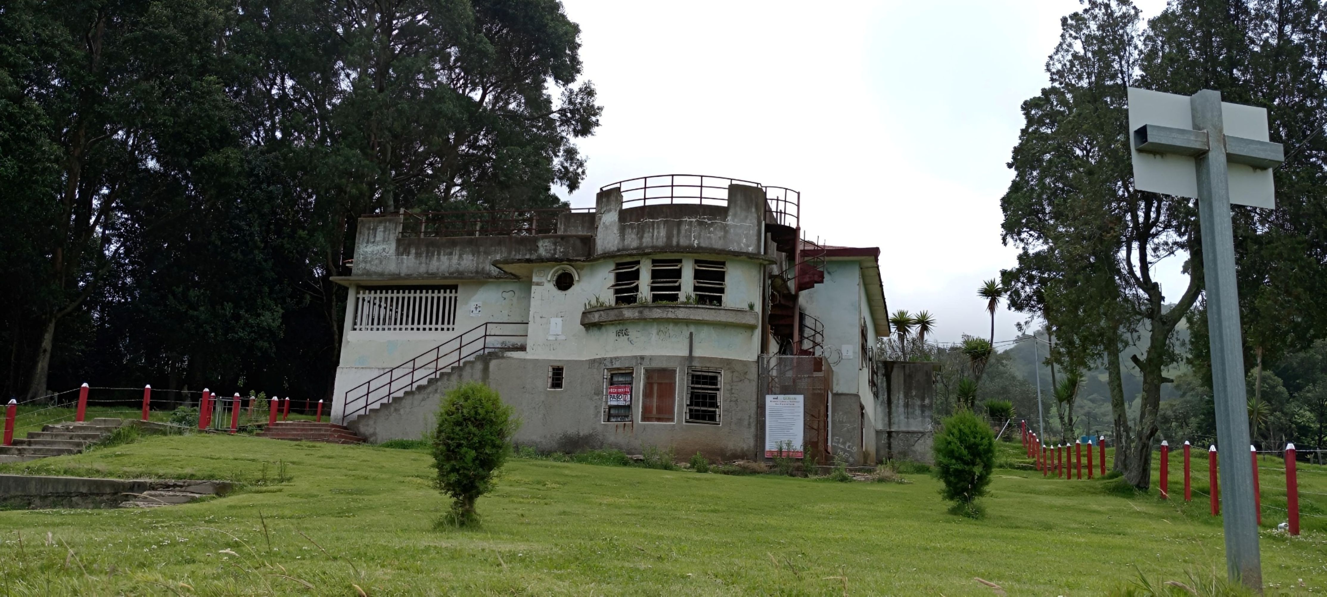 Circular tower of a former building at the Sanatorio Durán in Costa Rica, showing a rounded balcony and exterior staircase surrounded by trees.