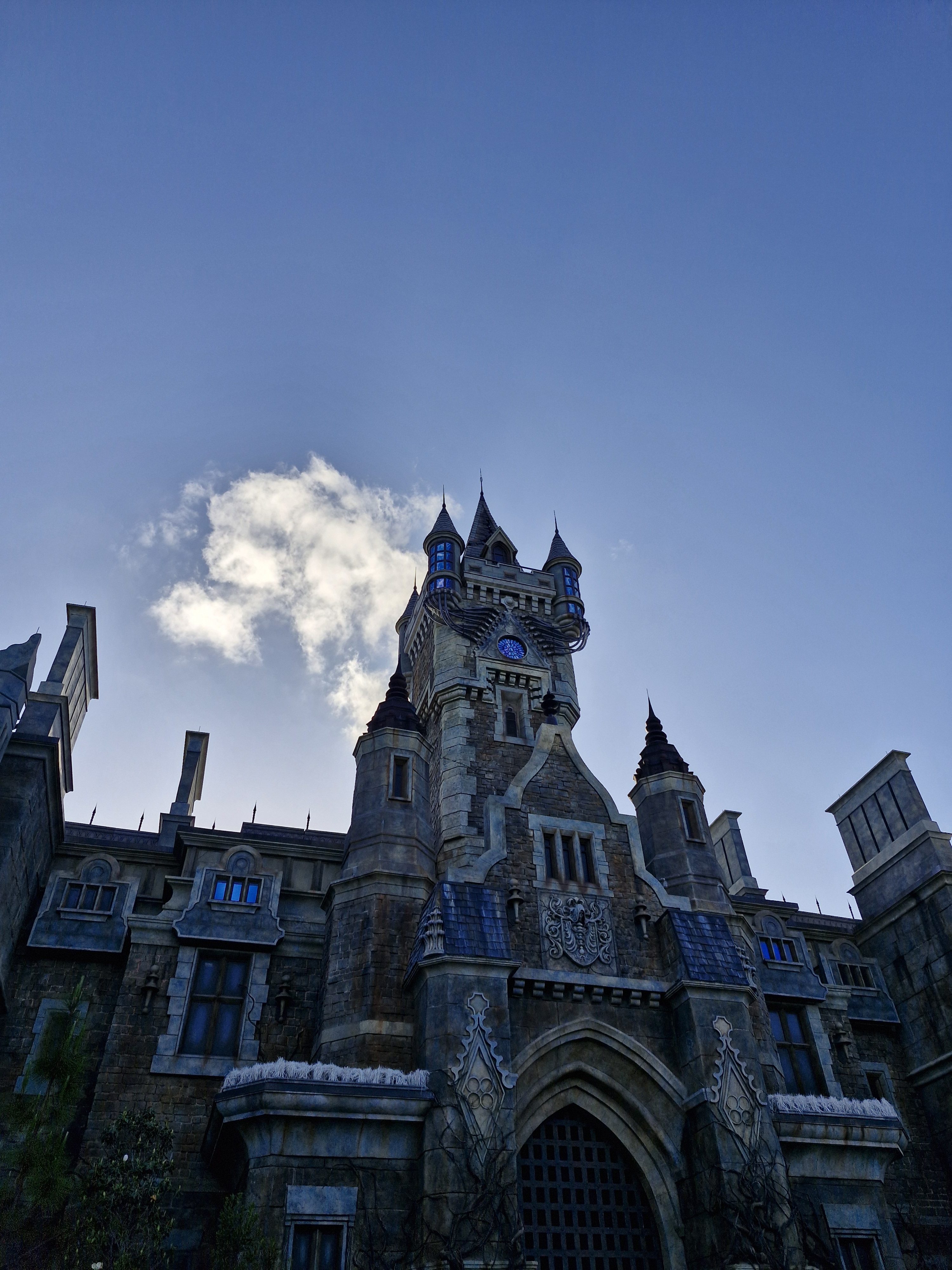 A grand castle with tall towers, stone walls, and an ornate entrance under a clear blue sky.