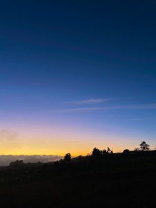 A serene twilight landscape where the sky transitions from deep blue at the top to vibrant hues of orange and yellow near the horizon. 