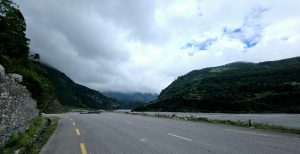 Winding road through lush green mountains under a cloudy sky.
