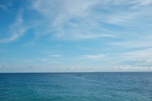 A small boat resting far out on a calm, deep blue sea under a clear sky with soft clouds.